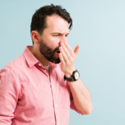 Un homme portant une chemise rose se couvre la bouche avec sa main, semblant vérifier la fraîcheur de son haleine.