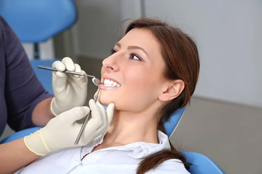 Une femme souriante assise sur une chaise dentaire reçoit un examen dentaire, le dentiste utilisant des instruments pour inspecter ses dents.