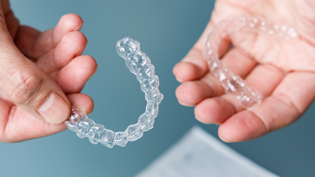 Gros plan sur des mains tenant des aligneurs dentaires transparents, utilisés pour l'orthodontie invisible.